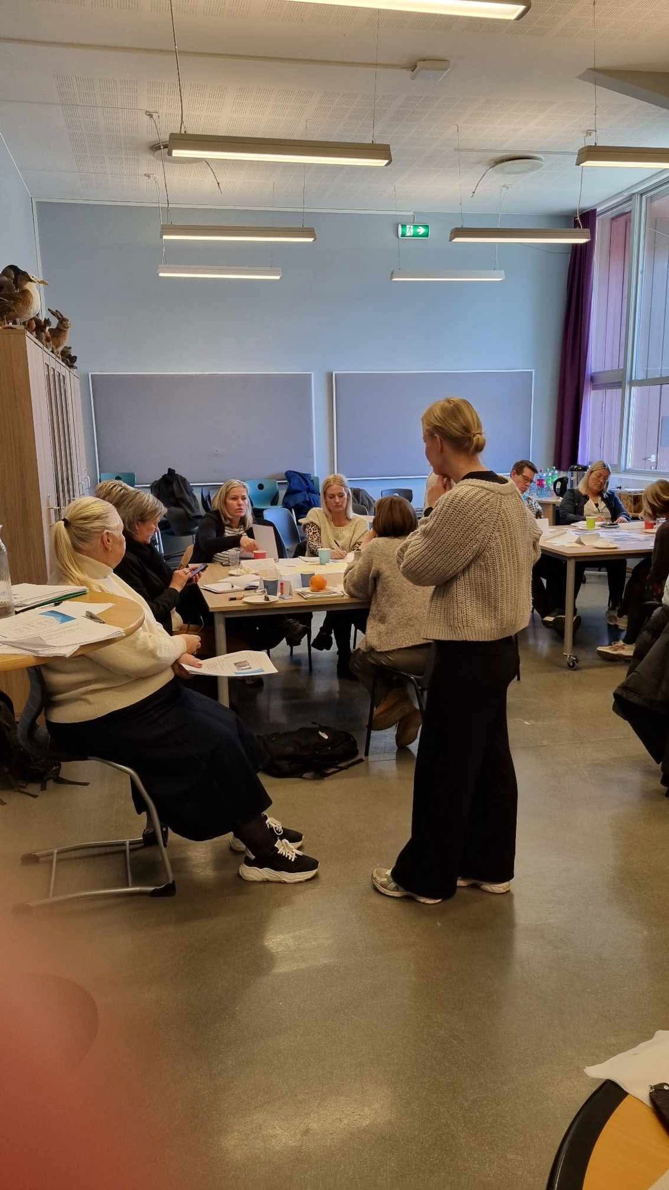 en person som står foran en gruppe mennesker som sitter ved bord en person som står foran en gruppe mennesker som sitter ved bord
